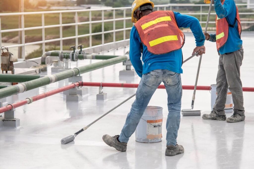 roofers-apply-roofing-silicone-to-roof A team of roofers applies silicone coating to a commercial roof to extend its life