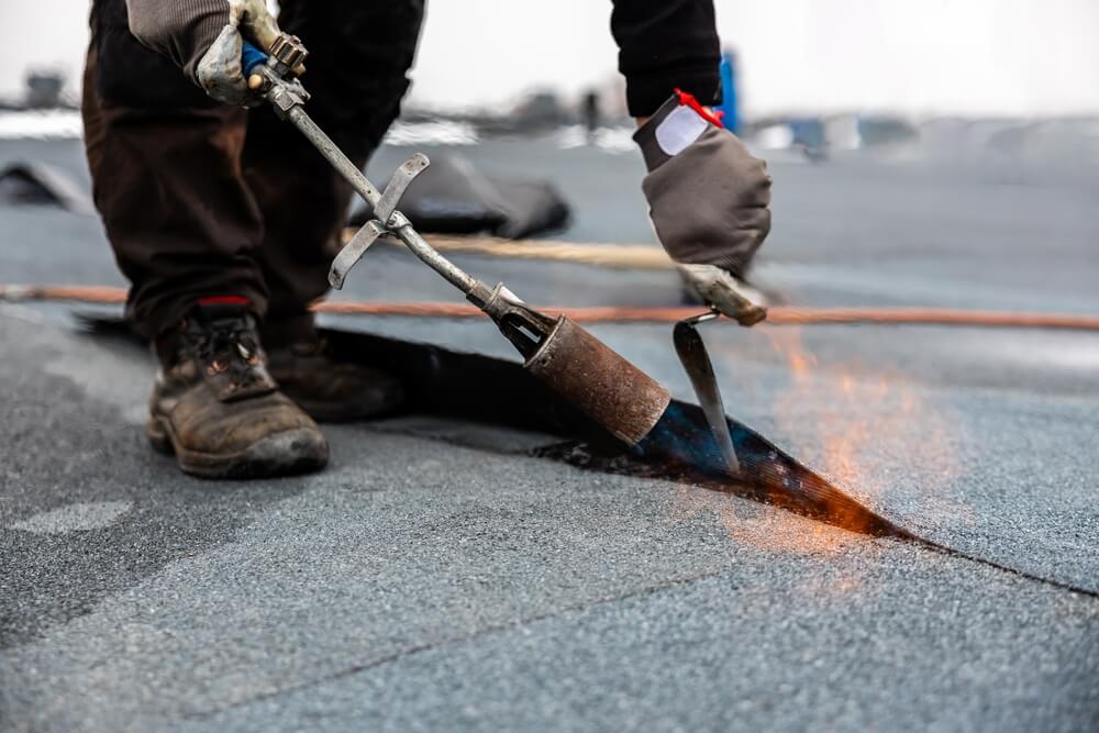 A roofing technician uses a torch to repair a flat roof seam