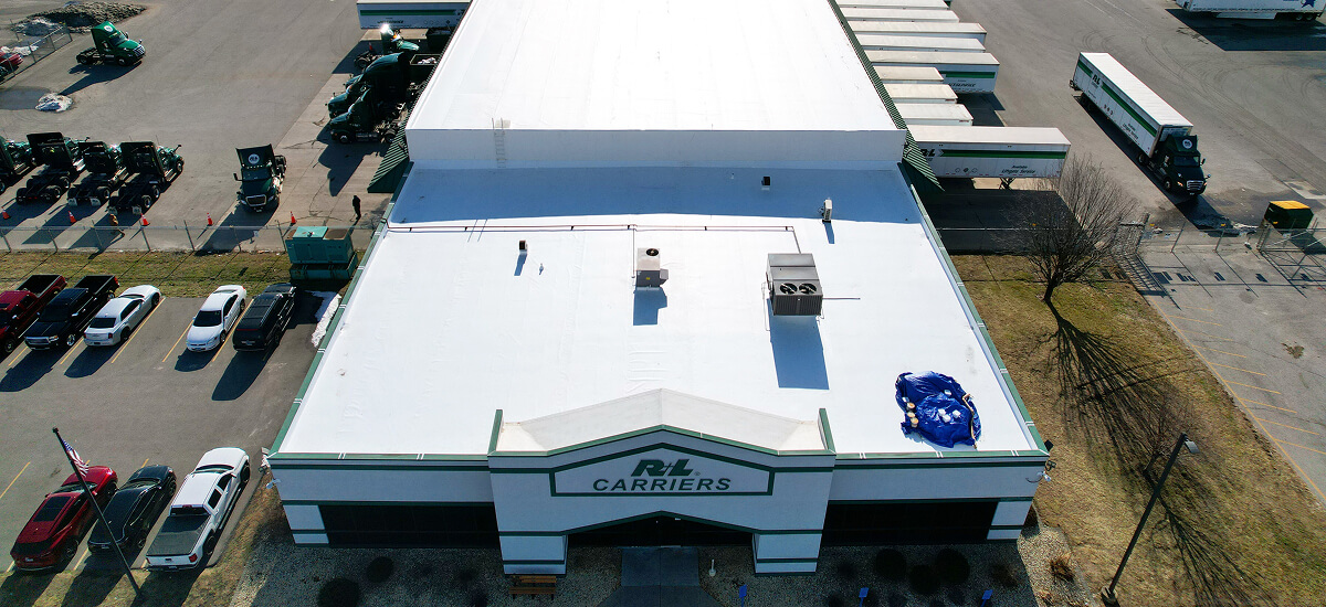 Aerial view of R+L Carriers facility with TPO flat roof, parked trucks, and commercial roof repair in progress.