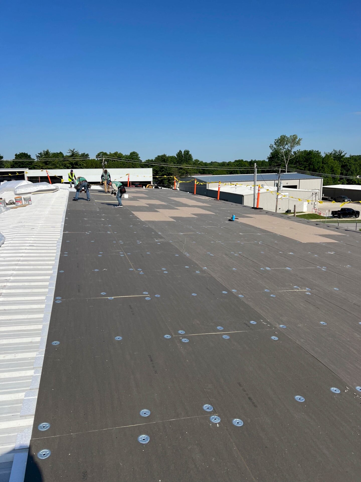 Technicians install TPO flat roofing and perform commercial flat roof restoration under clear skies.