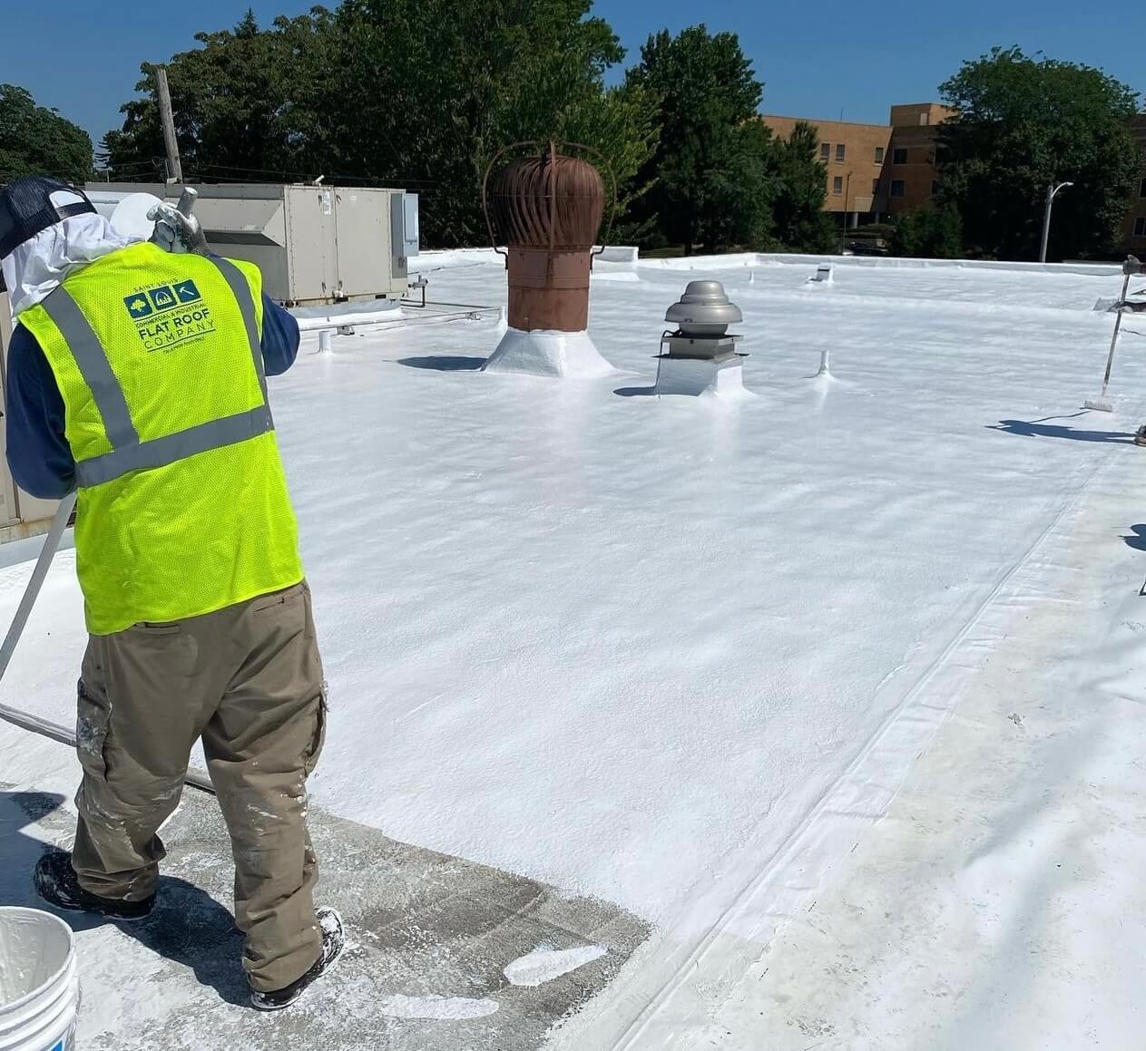 Technician in neon vest applies coating during TPO flat roof restoration and repair, HVAC visible.