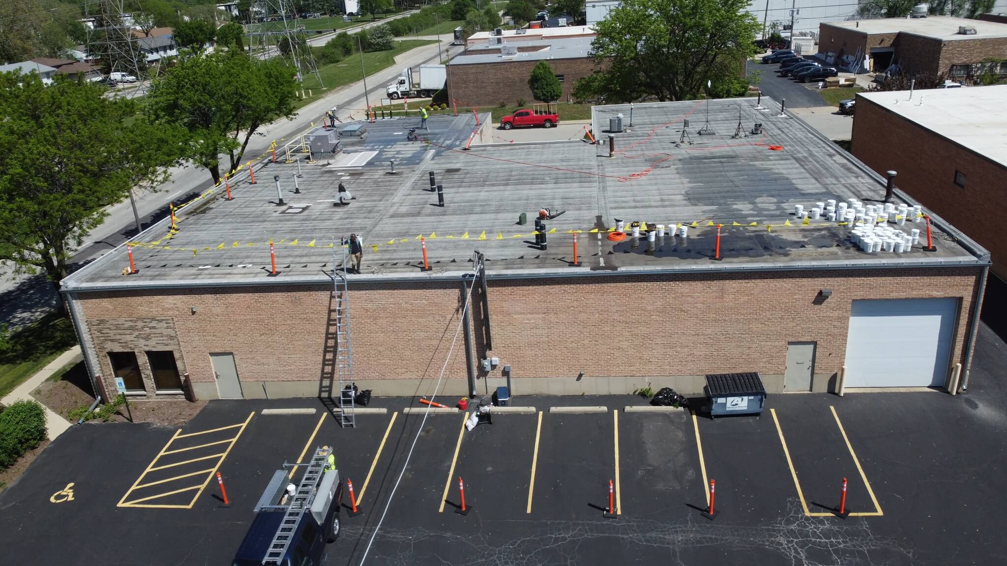 Aerial view of crew performing commercial flat roof repair, TPO restoration, and maintenance with safety barriers visible.