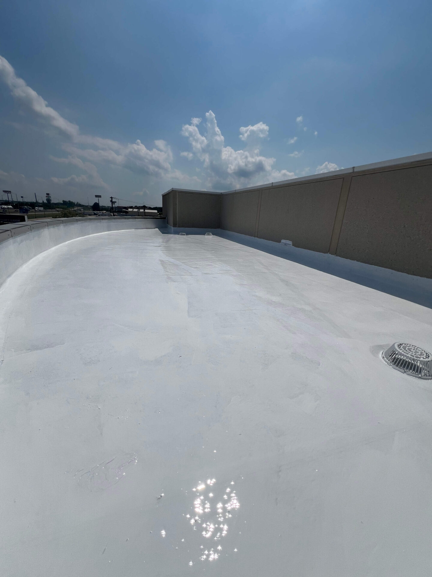 TPO flat roof with smooth reflective surface, beige parapet, and drain for commercial roof repair.