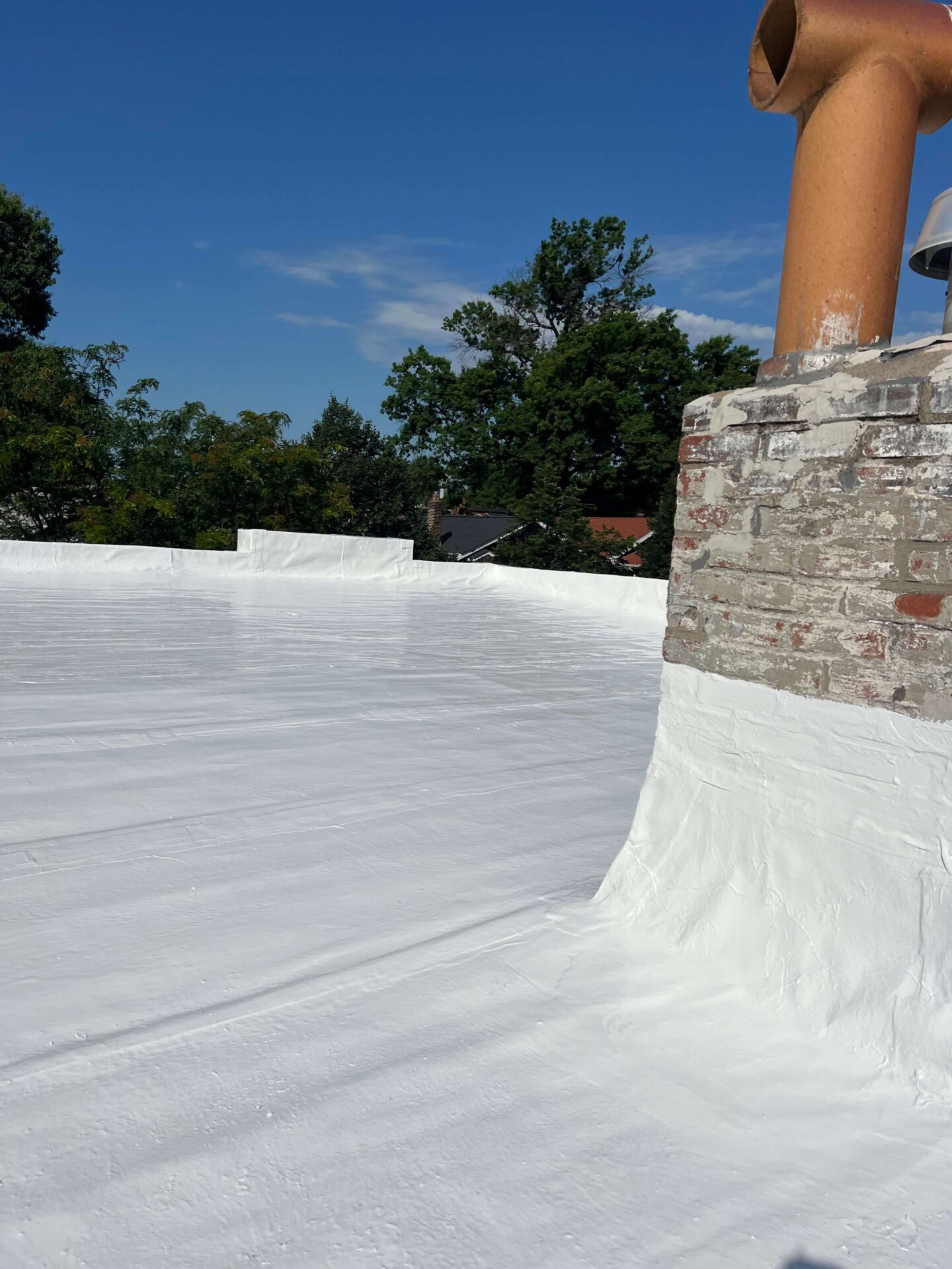 Commercial flat roof restoration with white sealant and brick chimney, ideal for flat roof repair and maintenance.
