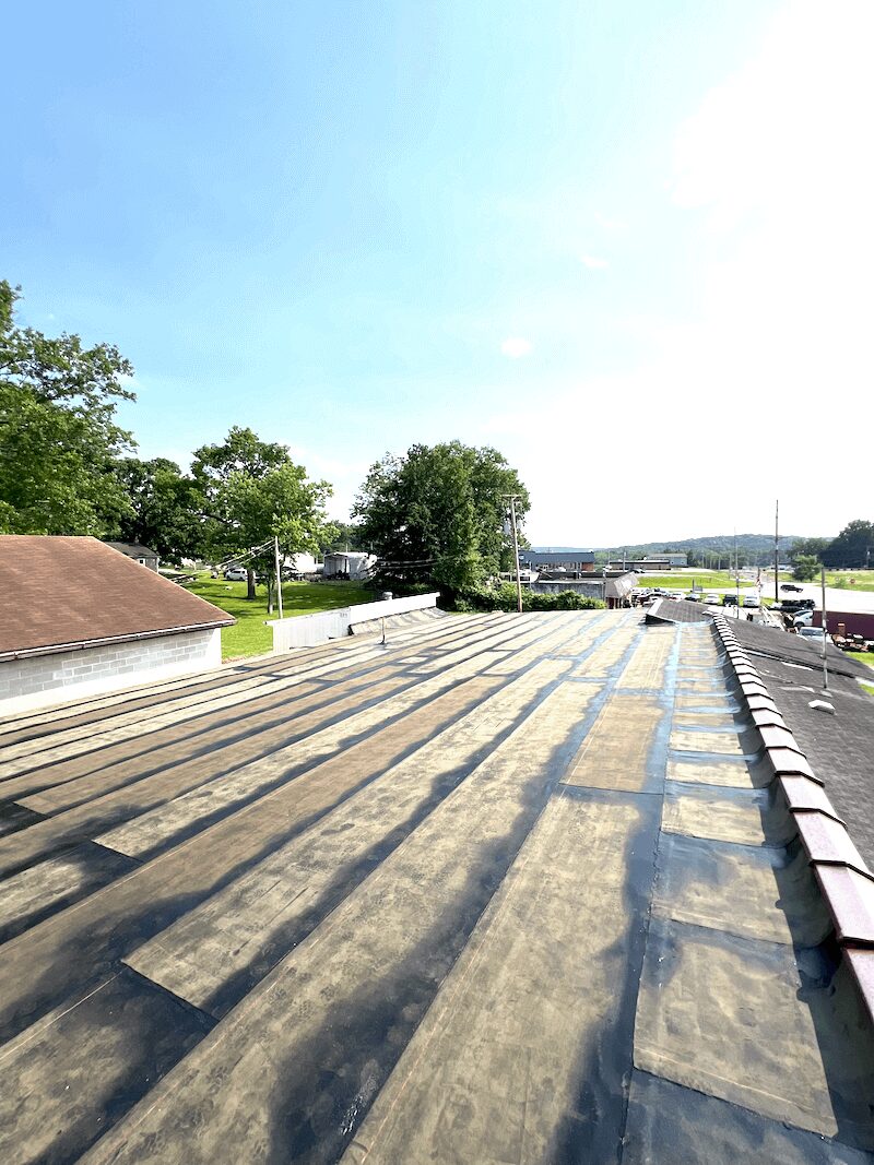 Commercial TPO flat roof with sunlit shadows, adjacent to metal roof, ideal for flat roof restoration and commercial roof repair.