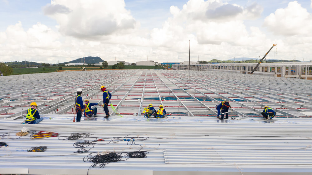 Teams of roofers install flat metal roofing on a large building