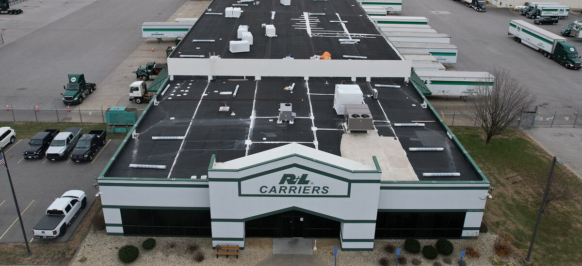 Aerial view of R+L Carriers warehouse featuring TPO flat roof and trucks at loading docks, ideal for commercial flat roof restoration.