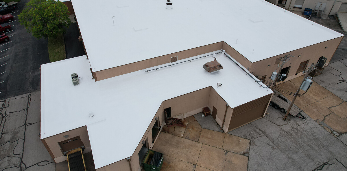 Aerial view of a tan commercial building with TPO flat roof, showing areas needing flat roof restoration and commercial roof repair.