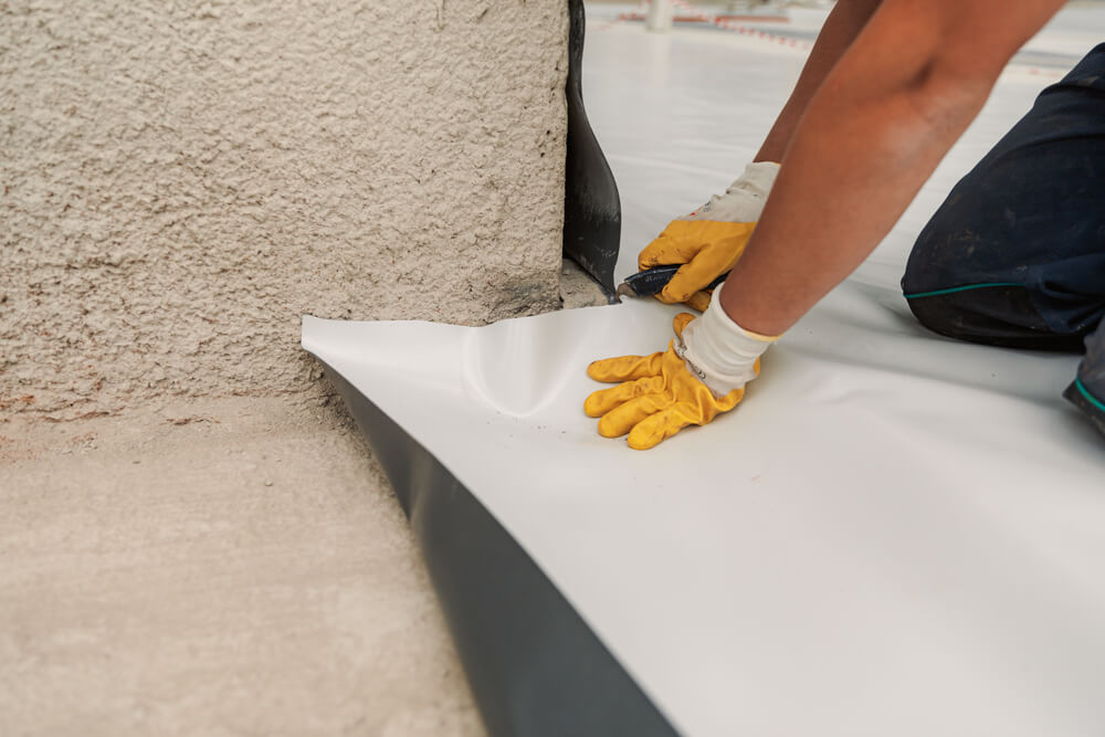 A roofer installs a single-ply roofing membrane around a corner