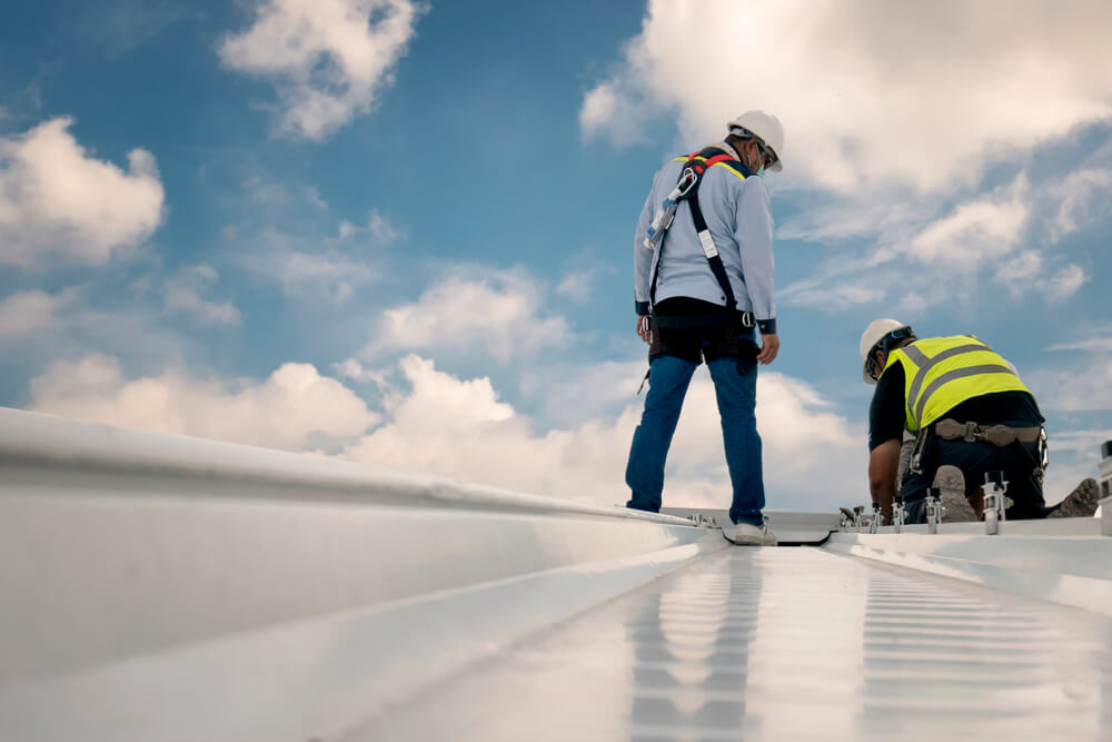 Two roofers repairing a flat metal roof on a commercial building