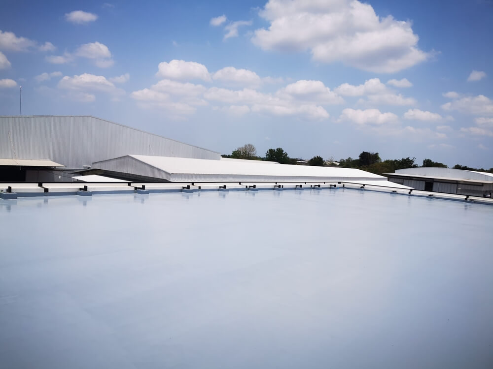 Flat commercial roof with reflective white membrane under blue sky