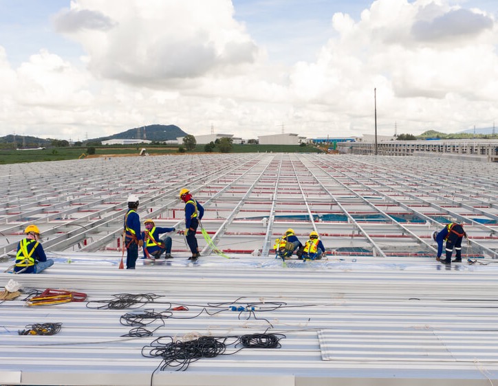 metal-roof-installation-industrial-building-construction-98 Commercial metal roof installation in progress on large industrial building with structural framing