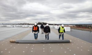 Commercial roofing crew installing a single-ply TPO roofing membrane on a large industrial building