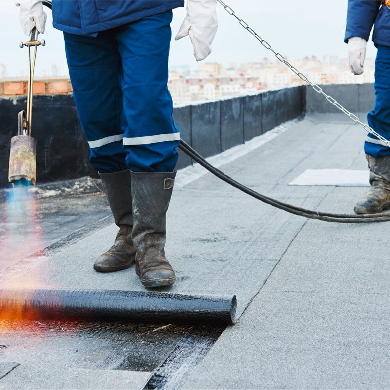 flat-roofing- Two workers torch TPO membrane in a commercial flat roof restoration project.