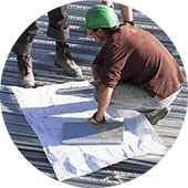 A worker inspects a commercial metal flat roof with TPO overlay blueprints.