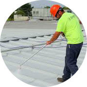 img-metal-roof-preparation Worker in neon shirt applies coating to commercial flat metal roof for flat roof restoration.
