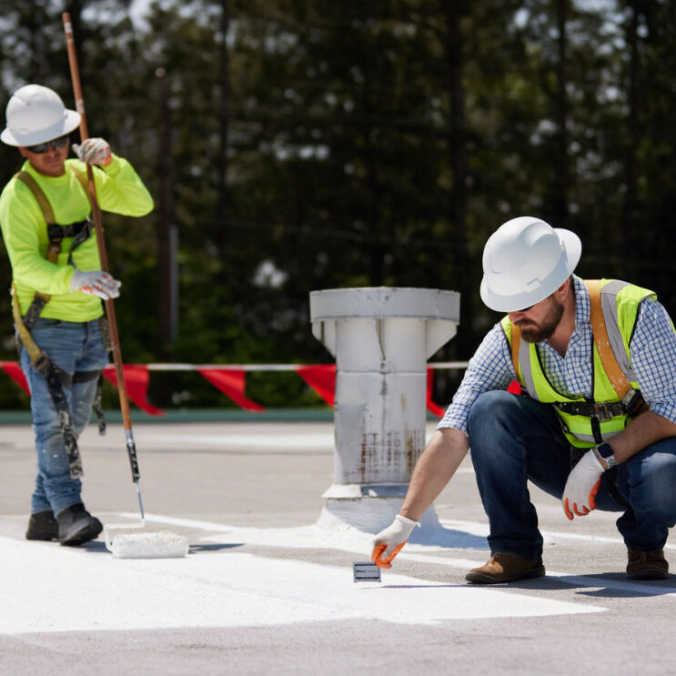 roof-restoration- Two workers in safety gear restore a commercial flat roof with TPO overlay in St. Louis.